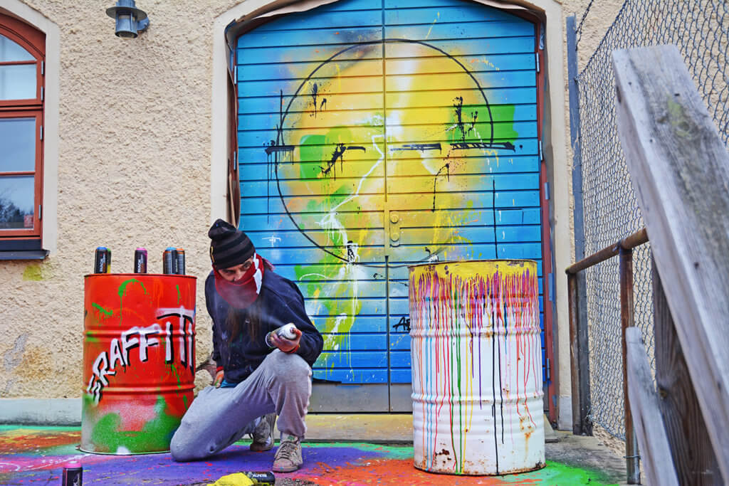 En man sitter på huk på en grafittimålad lastkaj och och håller i en sprayburk.